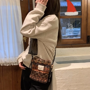 Detail of a vintage tweed crossbody bag in autumn tones worn by a model in a cozy room