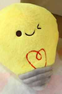 Close-up of cute yellow light bulb plush with embroidered heart filament and soft texture
