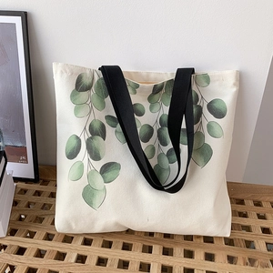 Detailed shot of canvas tote with green eucalyptus print on a minimalist wooden stand