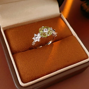 Macro detail of silver flower ring with green circular zircon and petal stones in a box