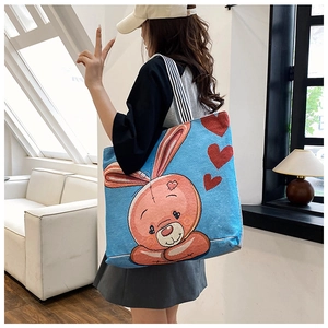 Detailed shoulder view of a blue canvas tote bag with pink rabbit embroidery and striped handles