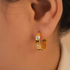 Close-up of gold geometric C-shaped earrings with inlaid zircons worn by a model