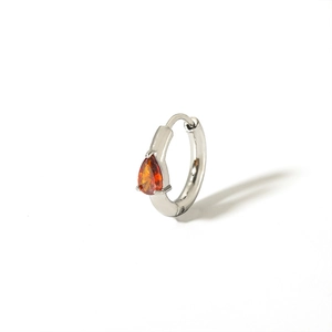 Macro detail of silver huggie earring with pear-cut orange zircon stone in prong setting