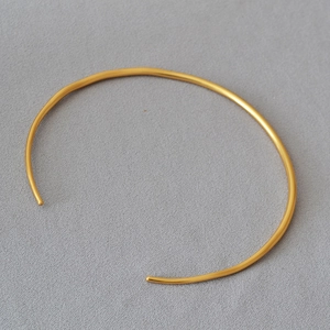 Minimalist gold plated C-shaped brass choker necklace on a light grey textured background