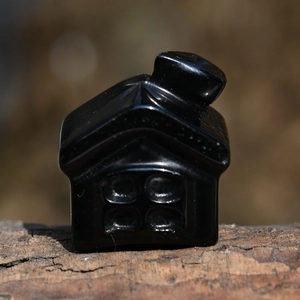Macro view of polished black obsidian stone house carving on a rustic wood base