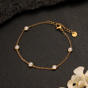 Close-up of gold stainless steel chain bracelet with bezel-set stones on textured leather