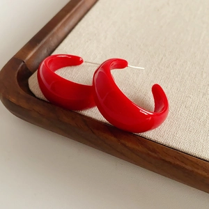 Macro shot of minimalist red C-shape hoop earrings on a wooden jewelry display tray