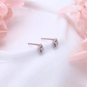 Detailed view of silver rhombic stud earrings with round zircon on white texture background