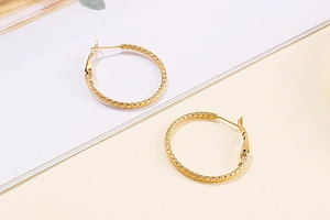 Detailed close-up of gold hoop earrings with fine textured metallic finish on white surface