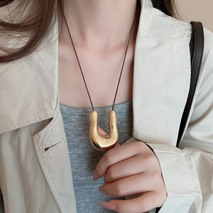 Ciondolo a U dorato irregolare su cordoncino scuro indossato da modella in cappotto