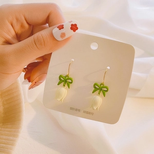 Detail of tulip pendant earrings with green bow accents and gold hooks on display card