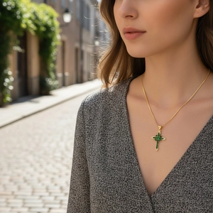 Detail of 18K gold cross necklace featuring green zircon stones on a female model