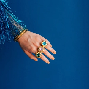 Close-up of gold rings with colorful square zircons worn on hand against blue background