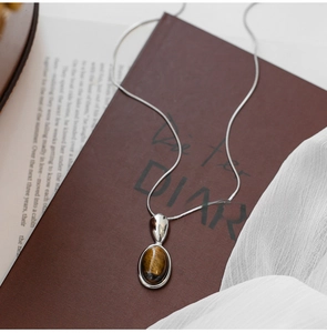 Macro detail of oval tiger eye stone pendant on polished silver-tone snake chain necklace
