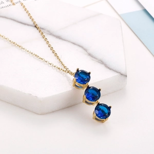 Dettaglio collana dorata con tre pietre preziose blu scuro su sfondo in marmo bianco
