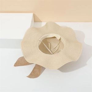 Detail of beige straw sun hat featuring unique wavy brim and brown ribbon on white blocks