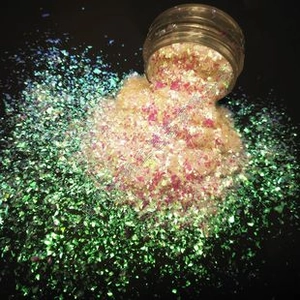 Macro shot of iridescent PET glitter flakes in a clear jar on black background