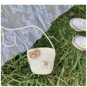 Detail einer weißen Strohtasche für Kinder mit Katzen- und Fischmotiven auf grünem Gras