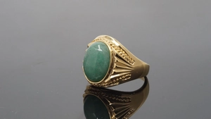 Detail of golden ring with oval green gemstone and braided texture on mirror background
