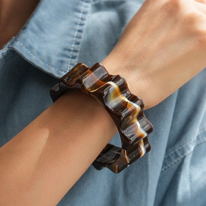 Primo piano di un largo bracciale rigido in resina ambrata con bordi ondulati su denim