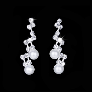Close-up of wedding earrings featuring sparkling crystals and white pearls on black background