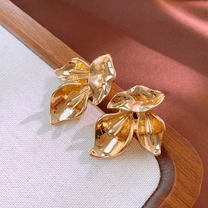Vue détaillée de boucles d'oreilles feuilles dorées sur plateau bois et fond en soie