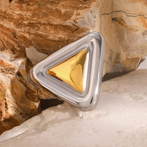 Close-up of geometric bicolored gold and silver metal brooch on a natural rock surface