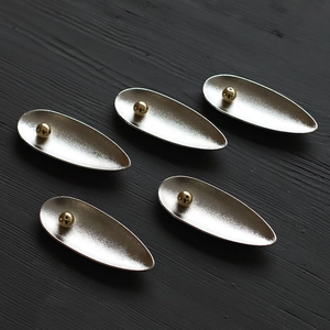 Detail of five teardrop-shaped metal incense holders in matte silver with gold bead centers