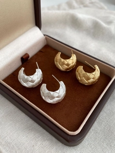 Detail shot of gold and silver woven C-shape earrings in a brown jewelry gift box