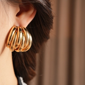 Close-up of golden multi-layer textured earrings on model with warm fabric backdrop