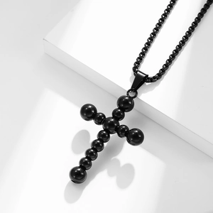 Minimalist black stainless steel beaded cross necklace on white geometric blocks