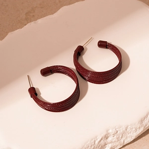 Close-up of wine red multi-layer C-shaped hoop earrings on a white stone tray