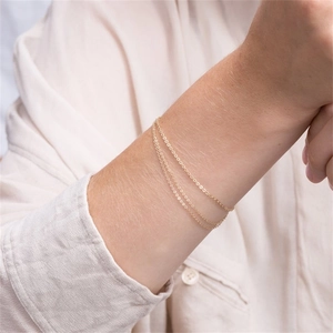 Close-up of a triple-layered minimalist gold chain bracelet worn on a model's wrist