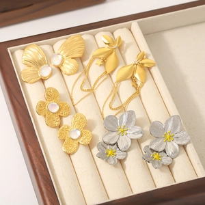 Eleganti orecchini in oro e argento con fiori e farfalle su un portagioie in velluto beige