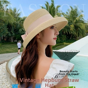 Detail of elegant straw hat with pink ribbon and bow against a beach resort background