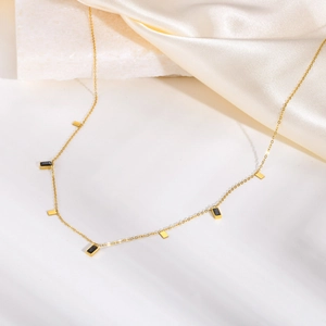 Detail view of gold station necklace with black stones on elegant white silk fabric