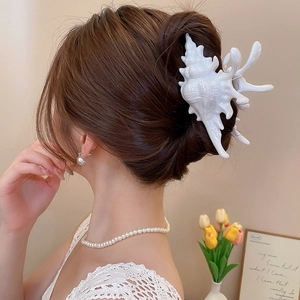 Close-up of shell-shaped acrylic hair claw clip worn with elegant pearl jewelry