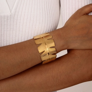 Close-up of a gold C-shaped cuff bracelet featuring an elegant leaf pattern on a model