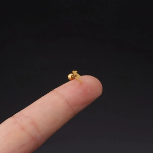 Macro shot of tiny gold stainless steel lightning bolt stud earring held on fingertip
