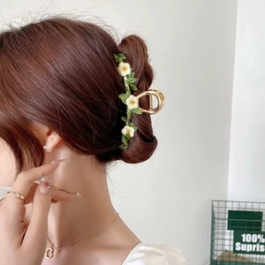 Detail of golden hair claw clip with white daisies and green leaves on a bun hairstyle