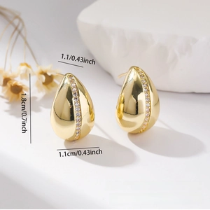 Detail view of gold water drop earrings with white zircon stones on stone background