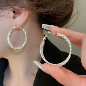 Macro detail of silver-toned textured round pendant earrings with a shimmering metallic finish