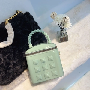 Detail of mint green jelly bucket bag with pyramid studs on white faux fur carpet