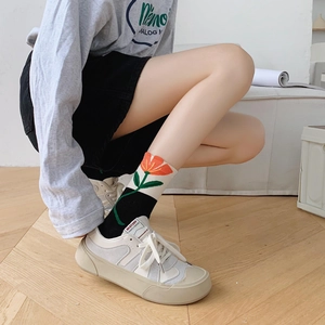 Detail of floral tulip mid-calf socks styled with beige platform canvas sneakers on wood
