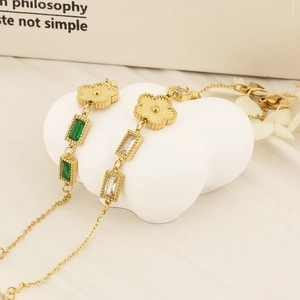 Detail of gold bracelets with green rectangular gems and floral pendants on white texture