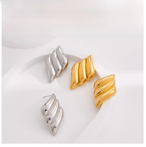 Detailed view of wavy gold and silver metal stud earrings with irregular pleated design