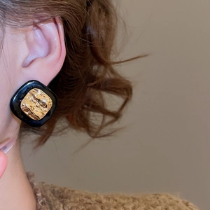 Close-up of vintage square black and gold studs with hammer texture on model's ear