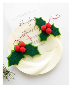 Detail of Christmas holly felt ornament with green leaves and red berries on a ceramic plate