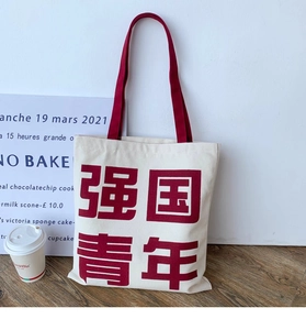 Close-up of white canvas tote bag with red handles and Chinese slogan on a wood floor