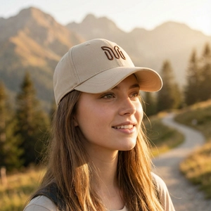 Stylish beige baseball cap with embroidered logo worn by a model in outdoor mountains.